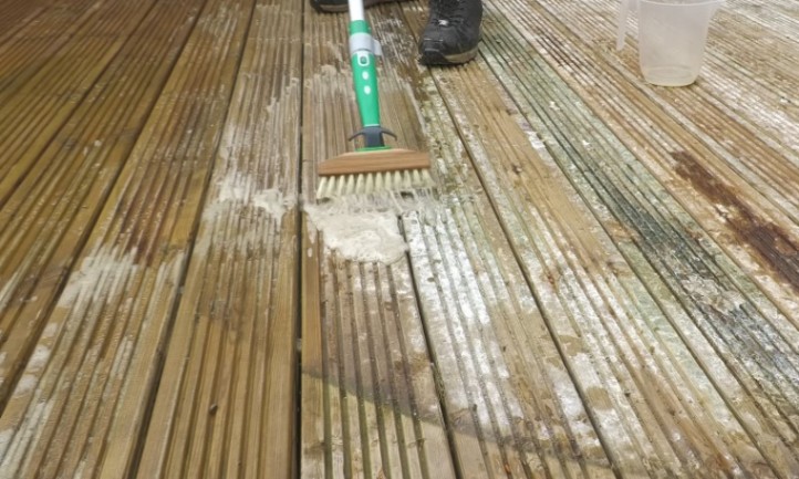 Person scrubbing a weathered wooden deck with a long-handled brush