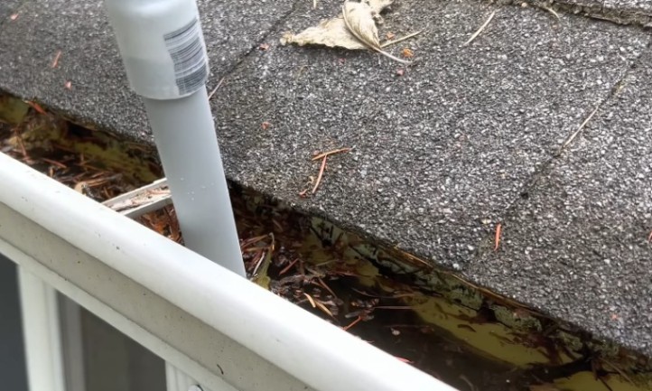 A clogged gutter being cleaned by the white pipe