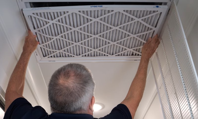 A man repairs a ceiling fan while holding a filter